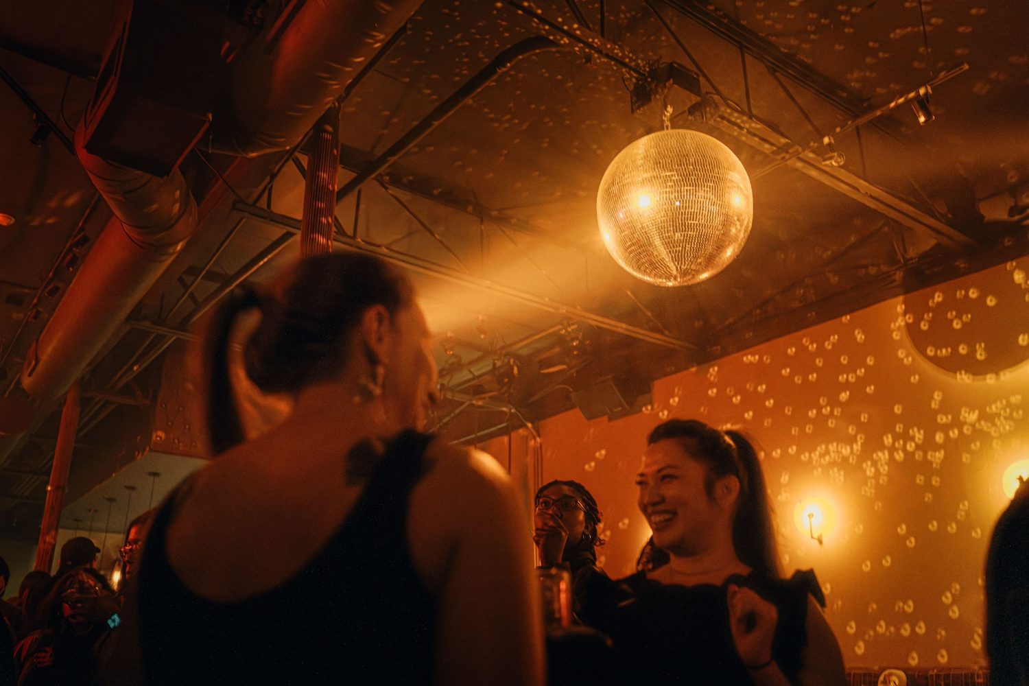 two women smiling at each other, disco ball, orange dim lighting