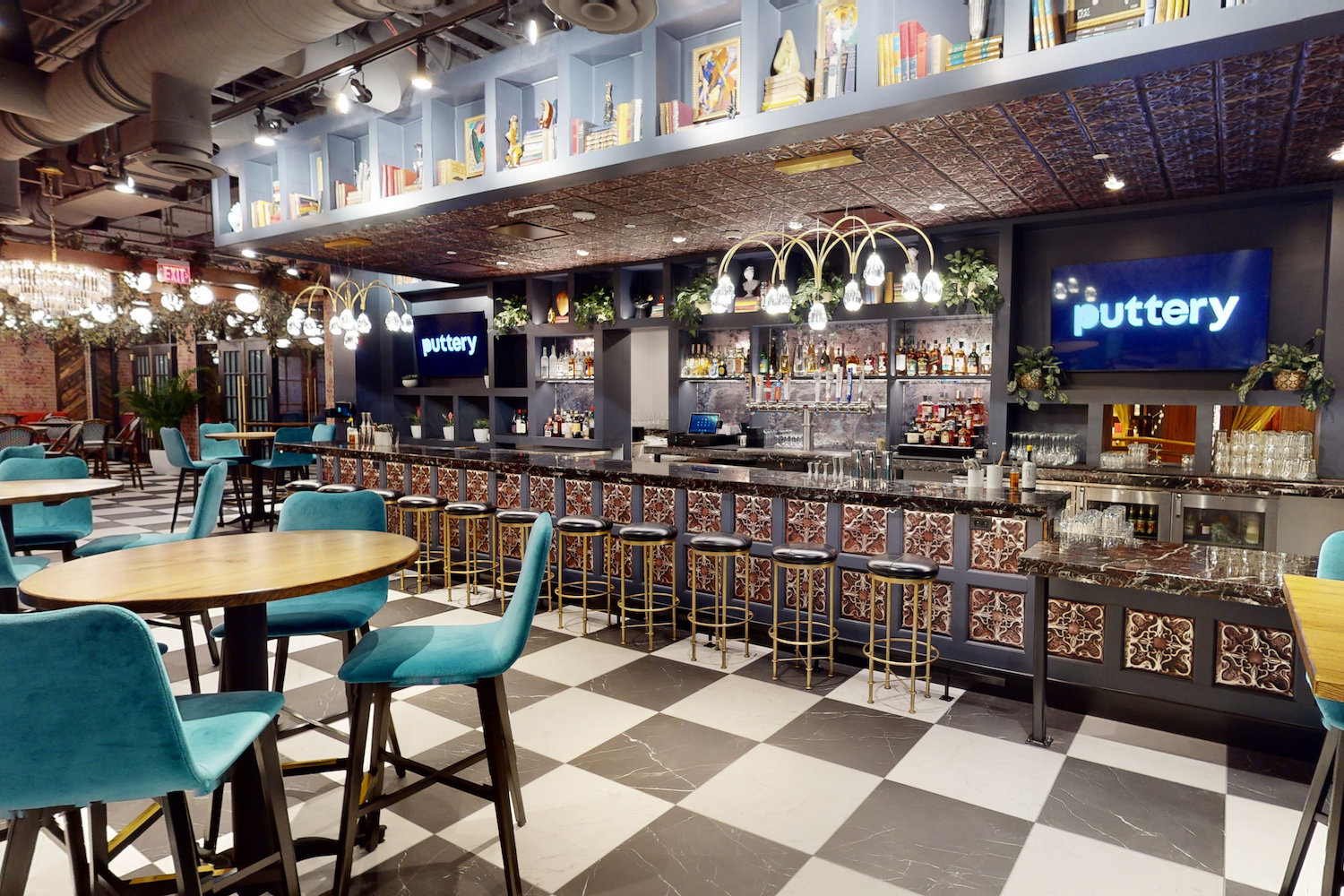 bar with two TVs, chandeliers, books, tables with teal chairs