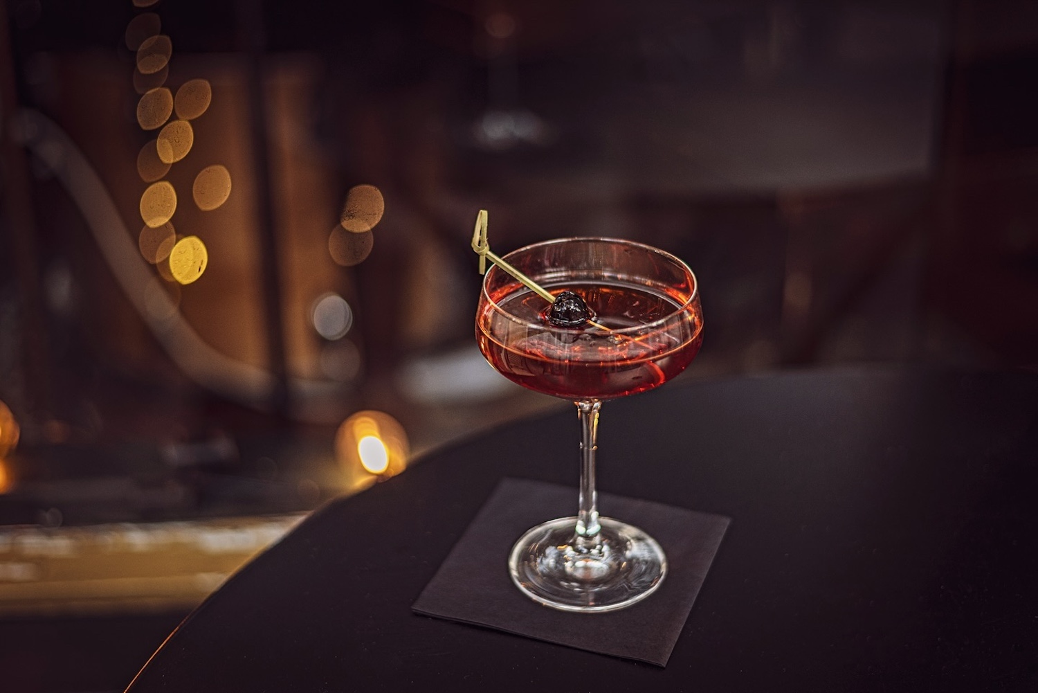 red cocktail with toothpick on a black napkin on black table