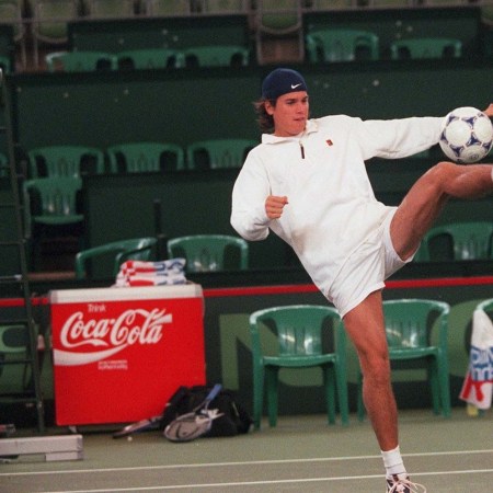 A tennis player kicking a soccer ball.