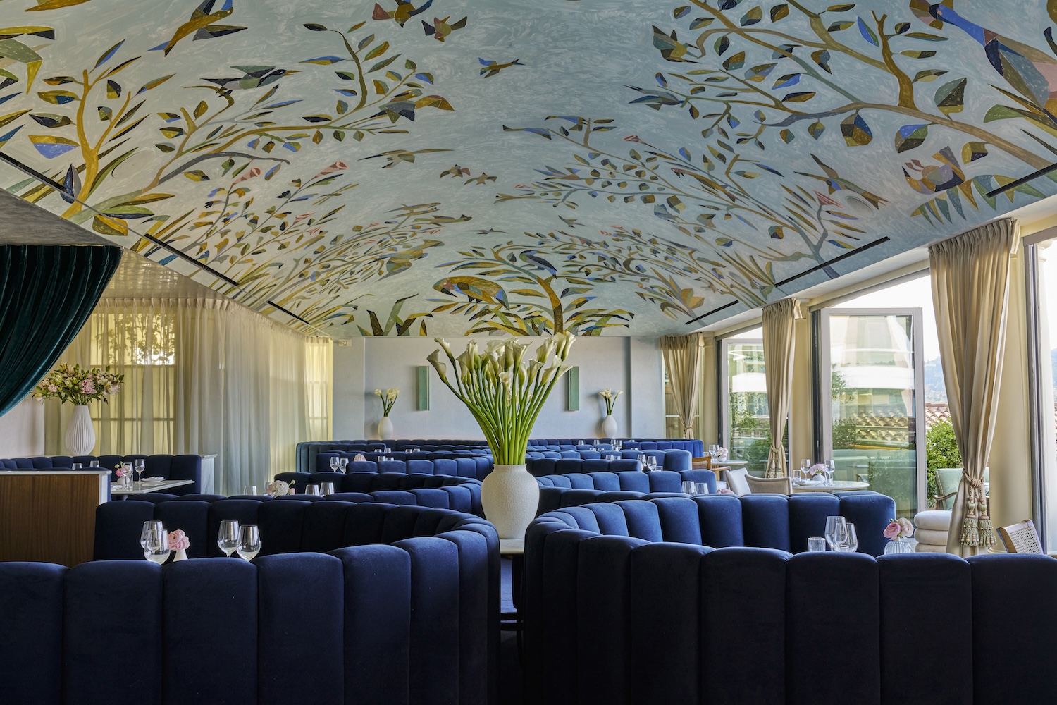inside of restaurant with navy booths and centerpiece plant, decorative wallpaper on ceiling