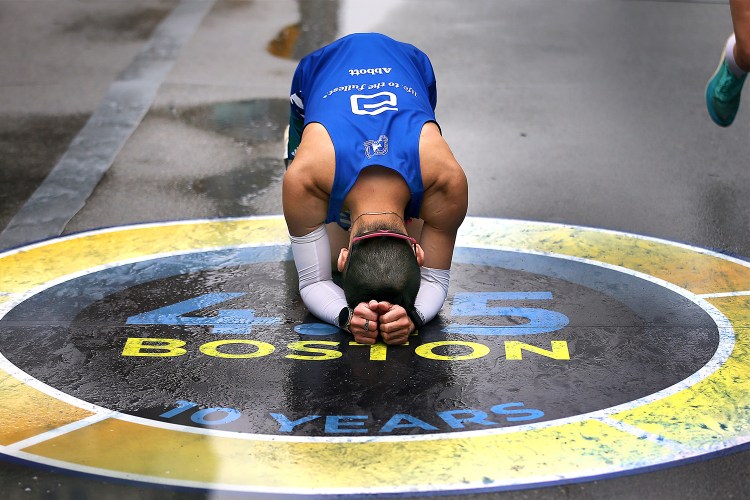 A man holds his head in his hands after completing the Boston Marathon.