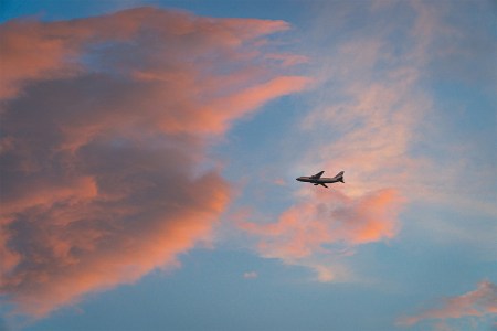 A plane passing through pink clouds during a sunset.