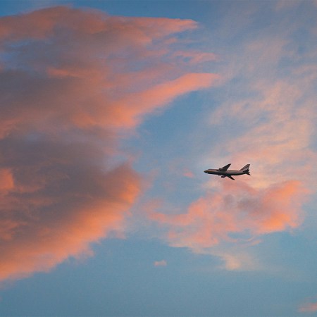A plane passing through pink clouds during a sunset.