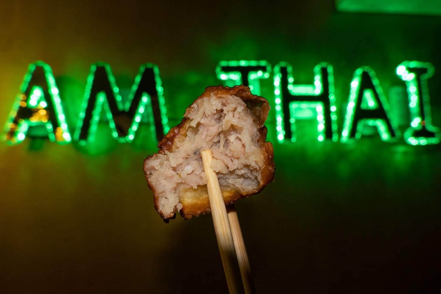 green neon sign with piece of meat on chopstick