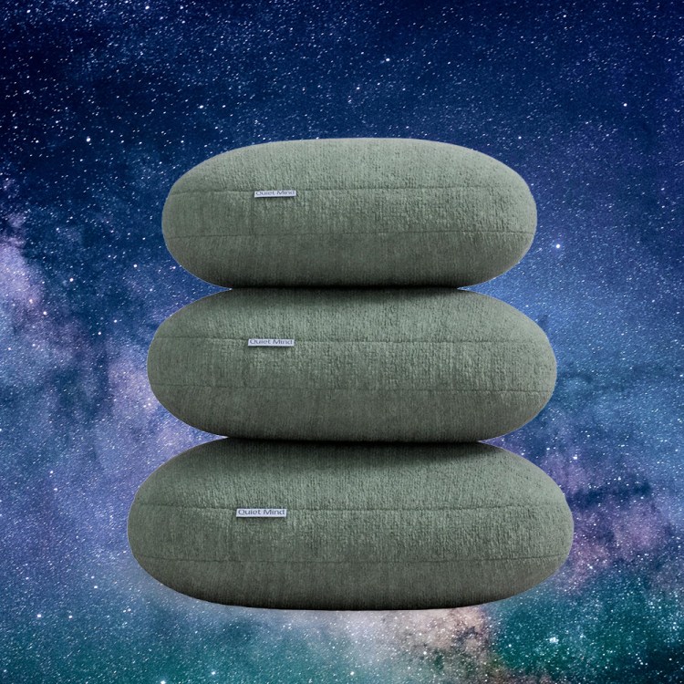 A pile of weighted pillows from Quiet Mind against a soothing cosmic background. Here's our review of their Original Weighted Pillow.