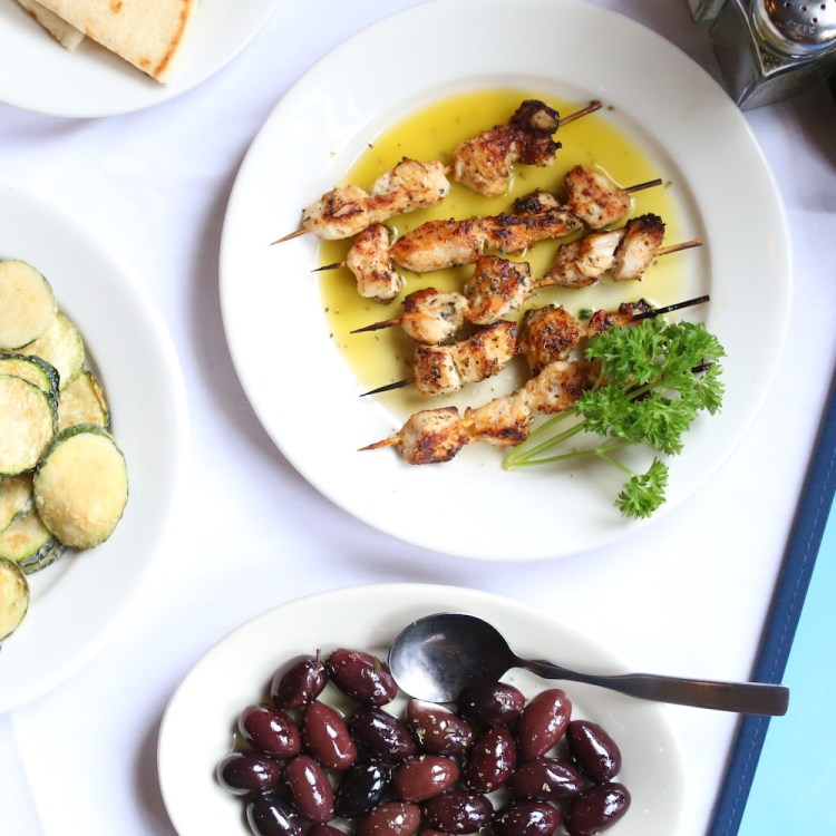 chicken kabobs, fried zucchini and kalamata olives on white plates sitting on a white tablecloth