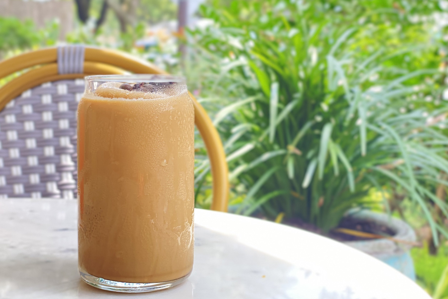 an iced coffee sitting on a white table with plants in the background