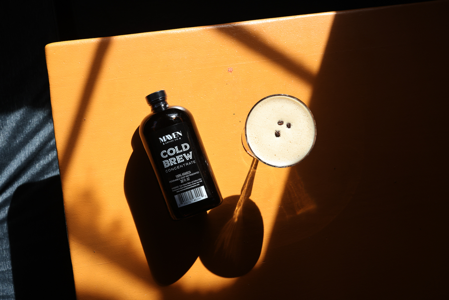 a bottle of maven cold brew next to an espresso martini on a yellow table with shadows