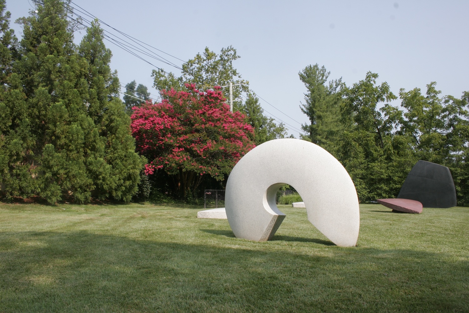 white round sculpture in a garden, trees, one red tree, grass