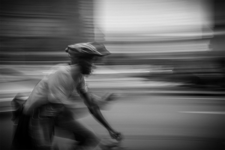 A man looking at his phone while riding a bike, black and white.