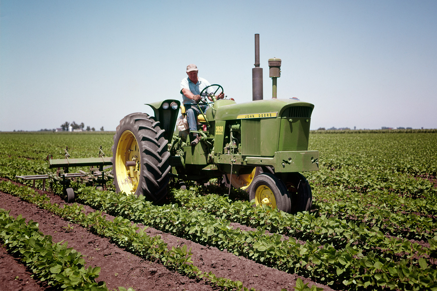 A vintage photo of a farmer driving a John Deere tractor through his fields.