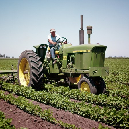 A vintage photo of a farmer driving a John Deere tractor through his fields.