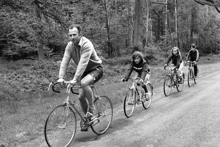 A man on a bike ride with three kids, black and white.