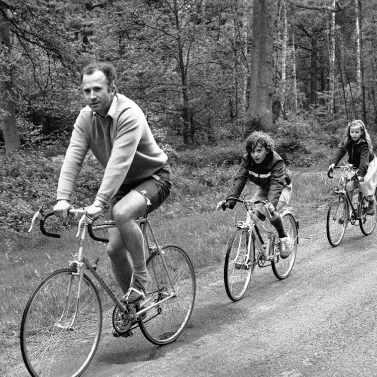 A man on a bike ride with three kids, black and white.