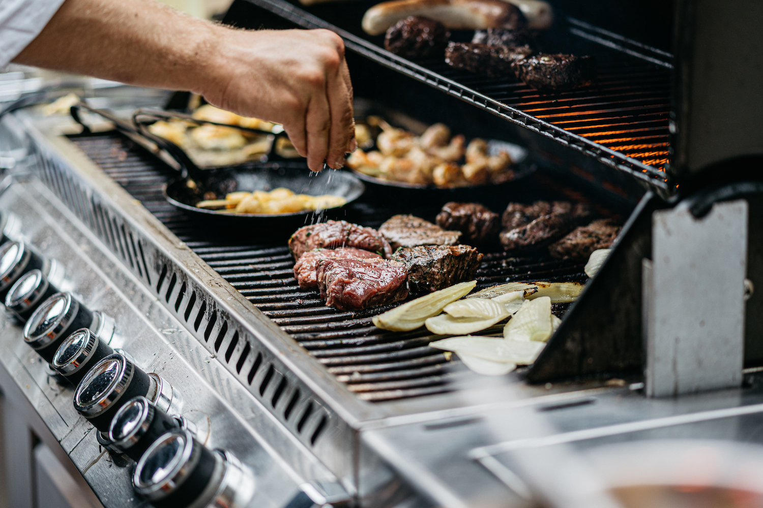 Human hand adds salt to the steaks on the grill