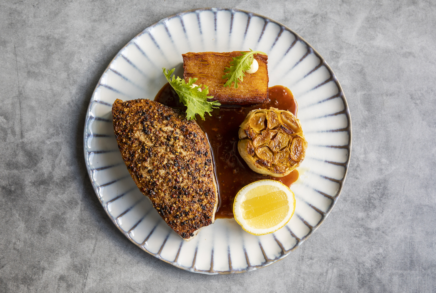 swordfish au poive, pomme anna and roasted garlic on a white plate on a gray table