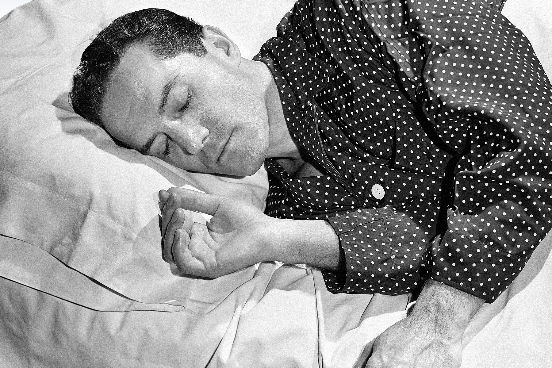 a black and white photo of a man sleeping in polka dot pajamas