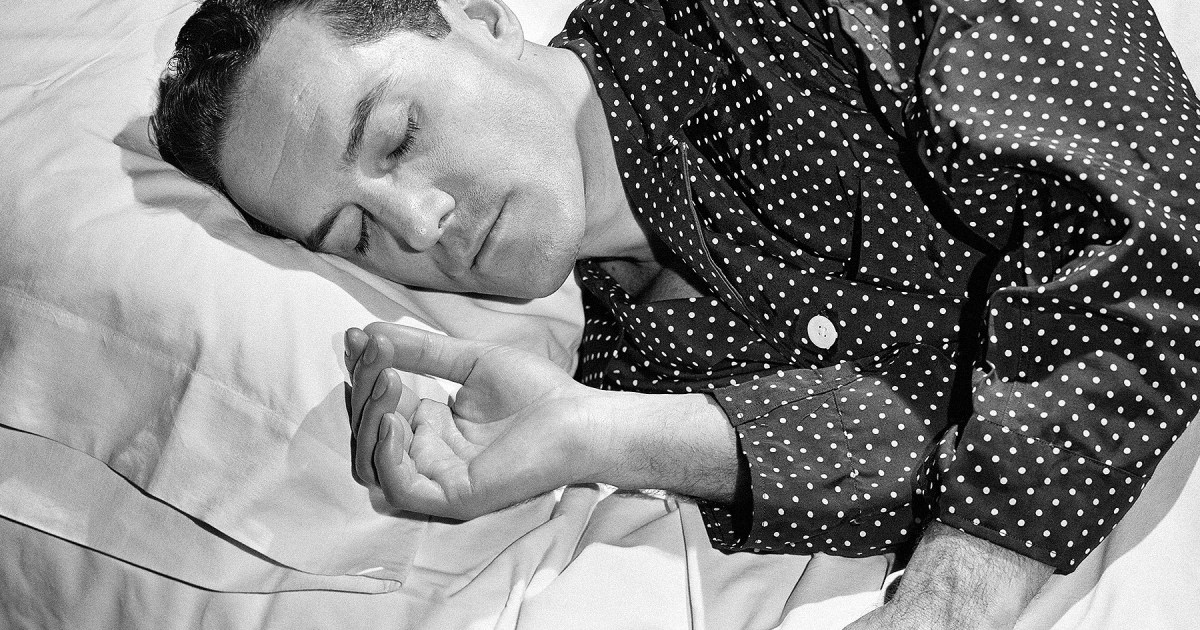 a black and white photo of a man sleeping in polka dot pajamas
