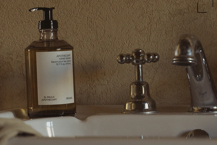 A brown glass bottle of "APOTHECARY HAND WASH" sits on a white sink next to a chrome faucet and tap.