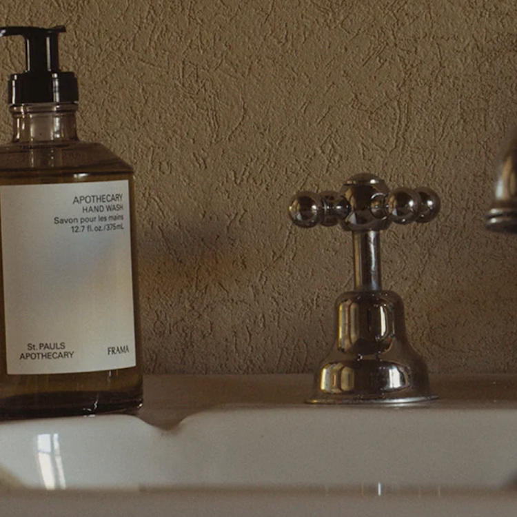 A brown glass bottle of "APOTHECARY HAND WASH" sits on a white sink next to a chrome faucet and tap.
