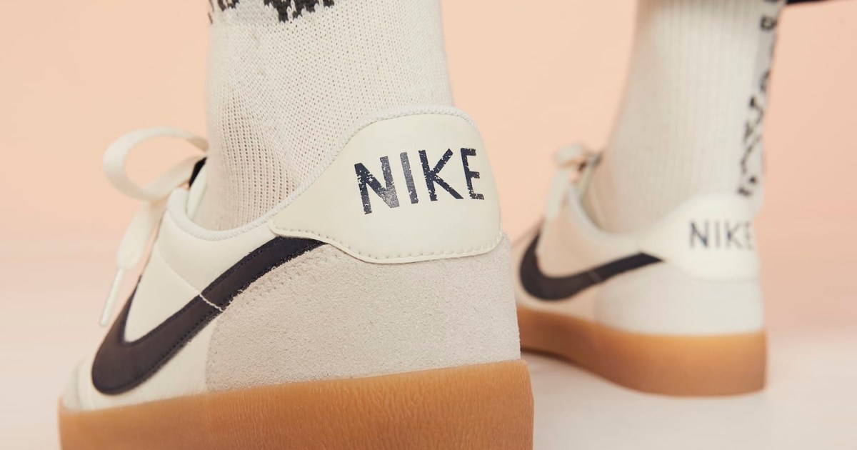 A man wearing grey, white and tan Nike sneakers seen from the back with the word "NIKE" emblazoned on the heel