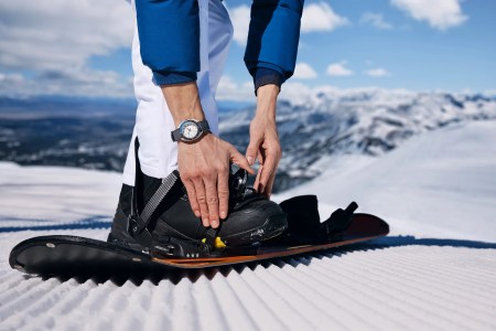A man wearing a Bulova Snorkel watch while putting on his snowboard boots on a mountain