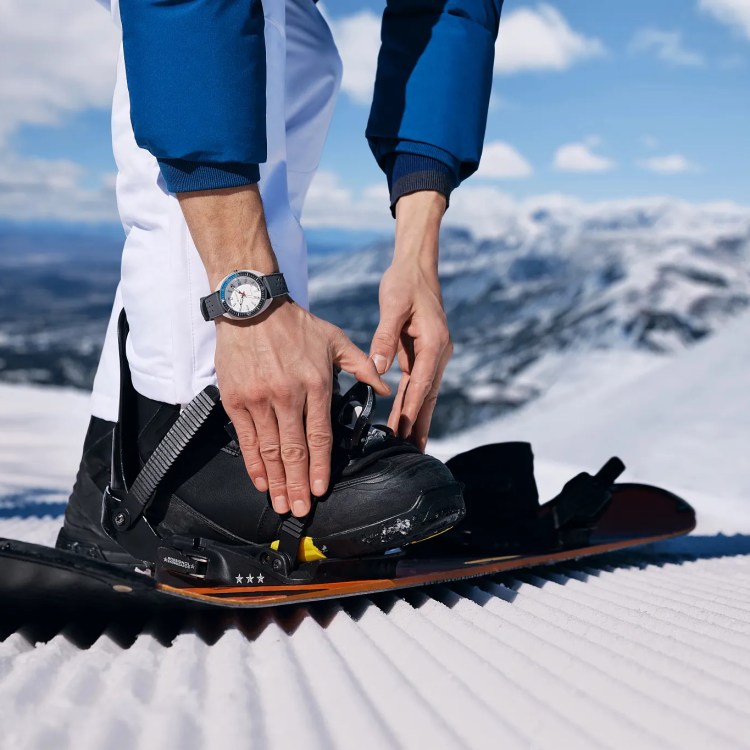 A man wearing a Bulova Snorkel watch while putting on his snowboard boots on a mountain