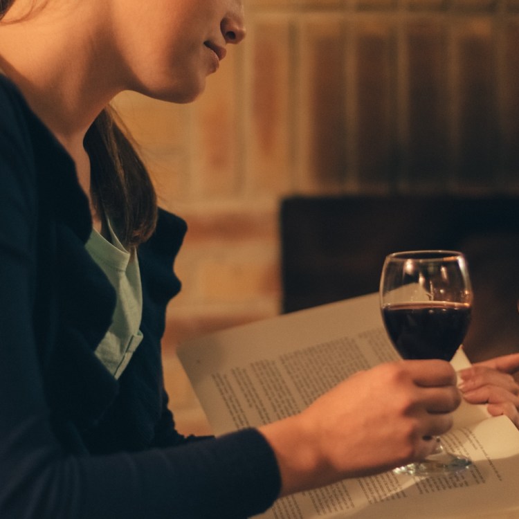 Woman near the fireplace reading a book with a glass of wine