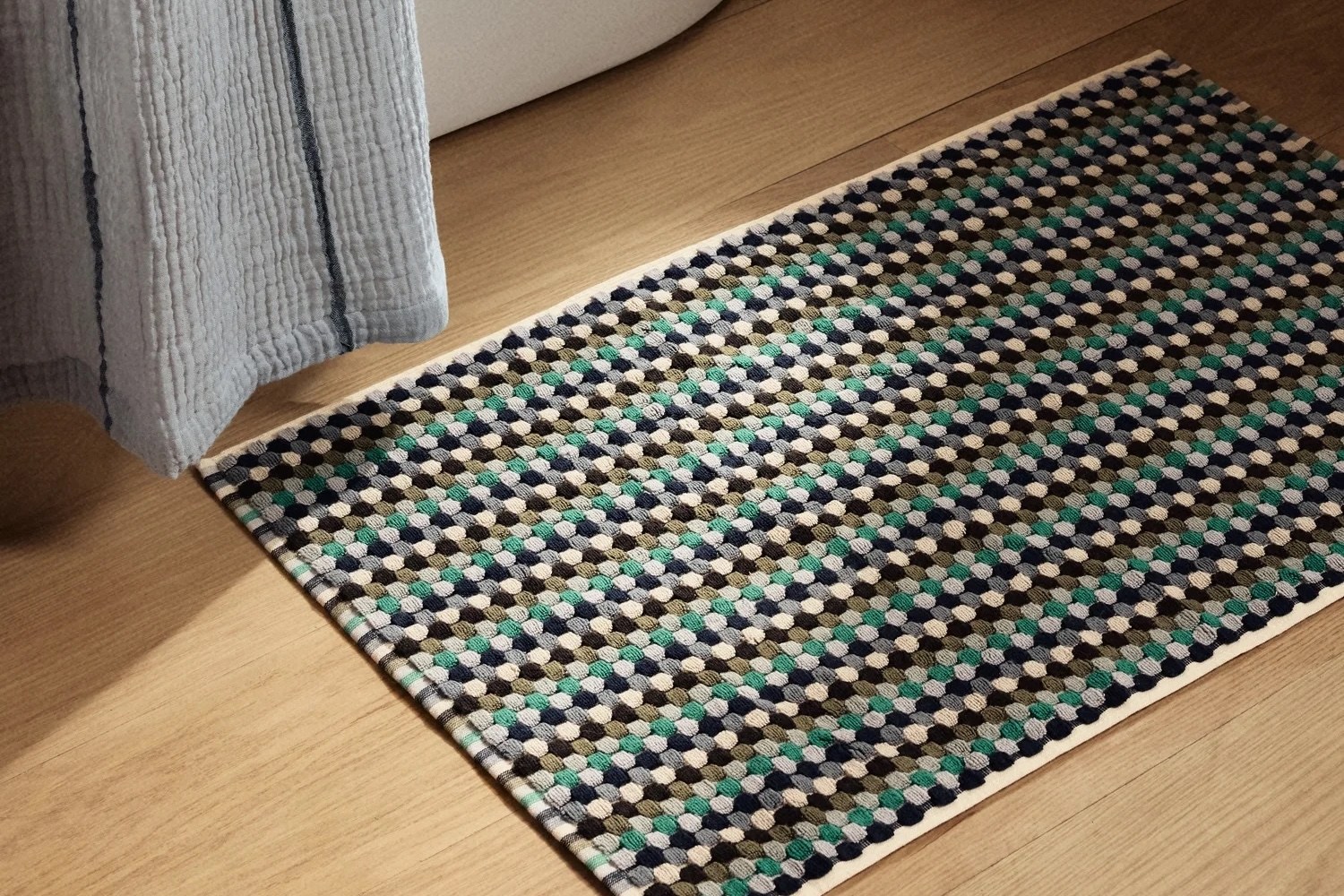 Textured bath mat with a repeating pattern of small, colorful circles in shades of blue, green, gray, and white on a light wooden floor.