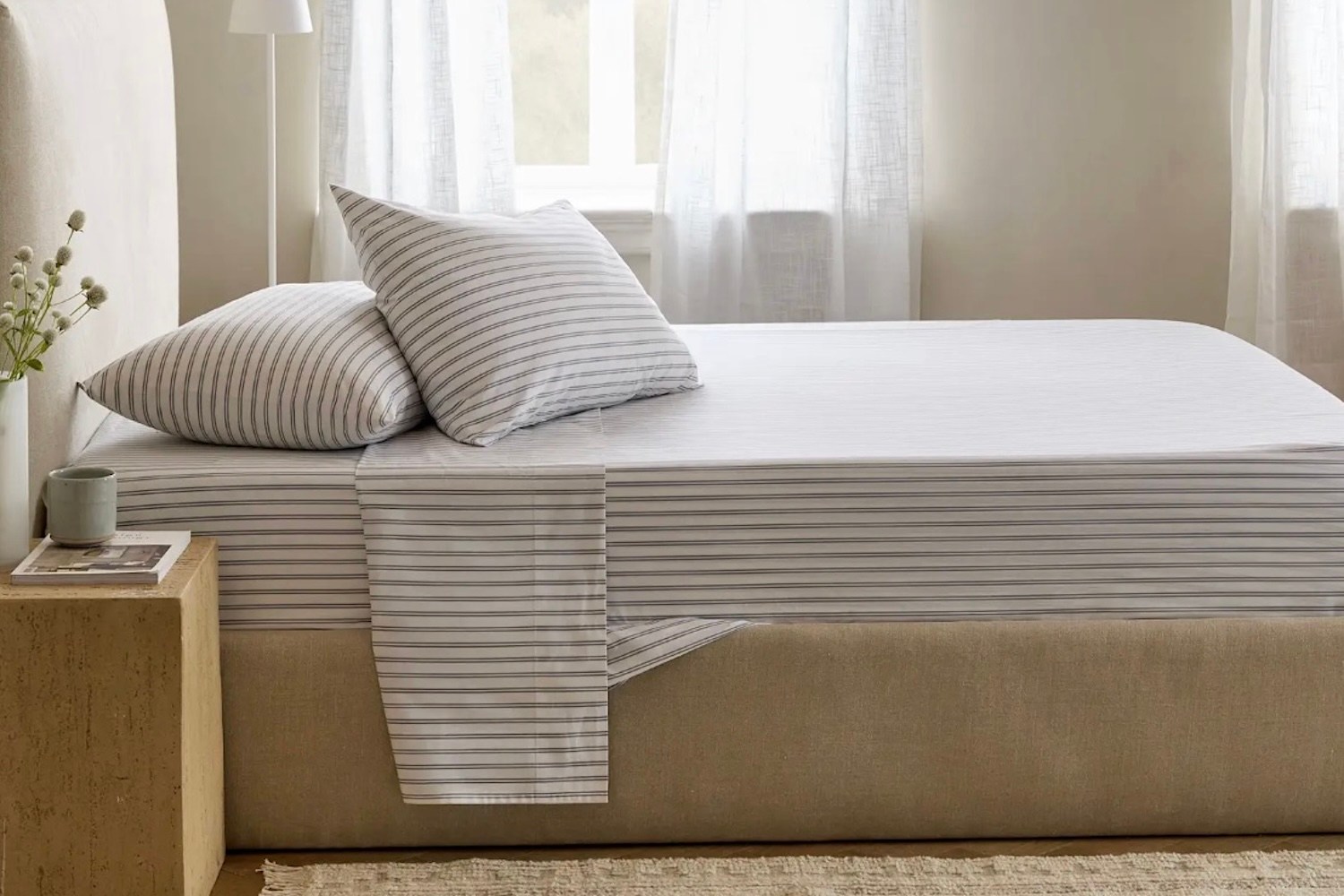 A bed with a beige headboard and base, covered in white sheets and two pillows with thin gray horizontal stripes.