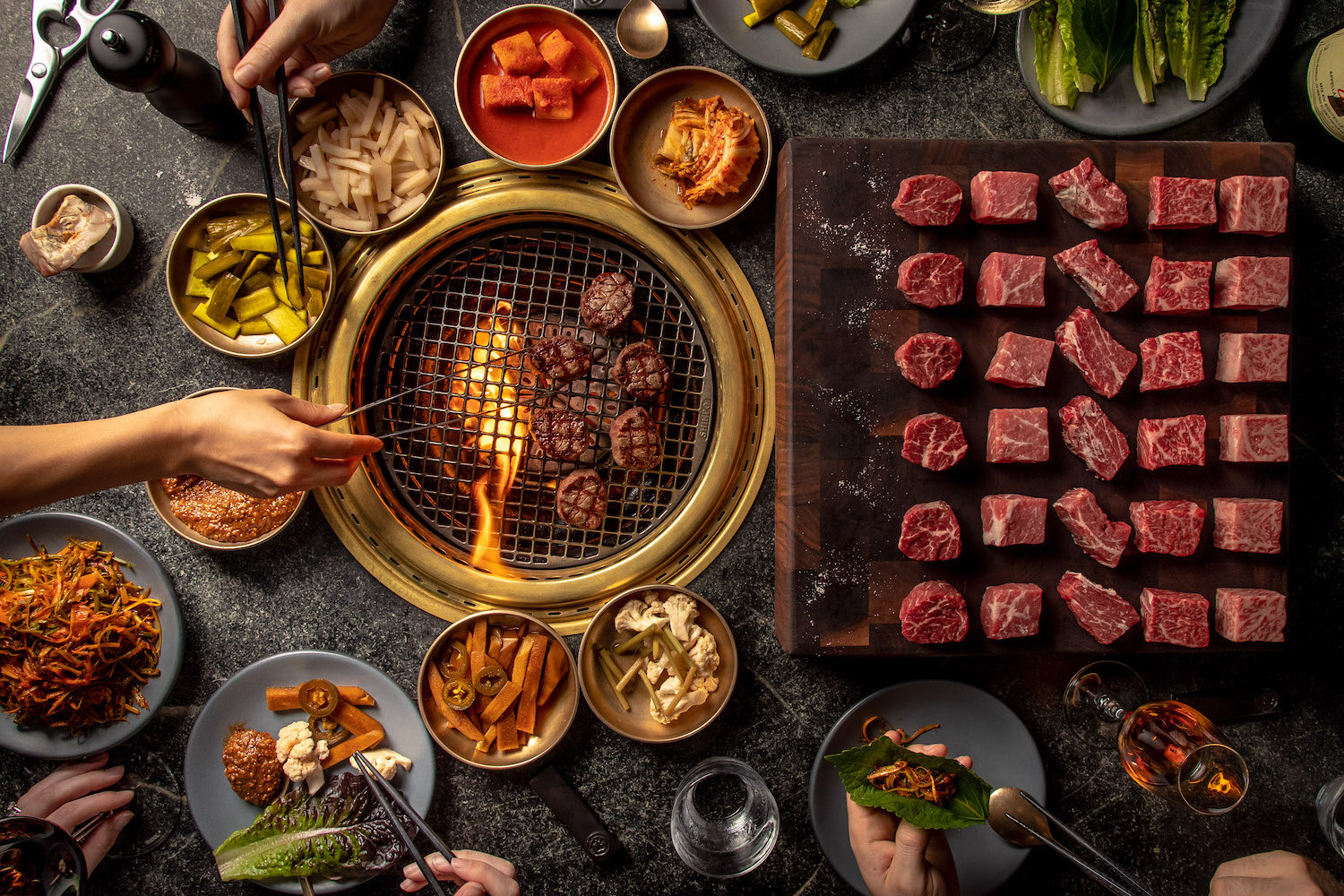 a tabletop grill at a korean steakhouse with marbled beef and banchan