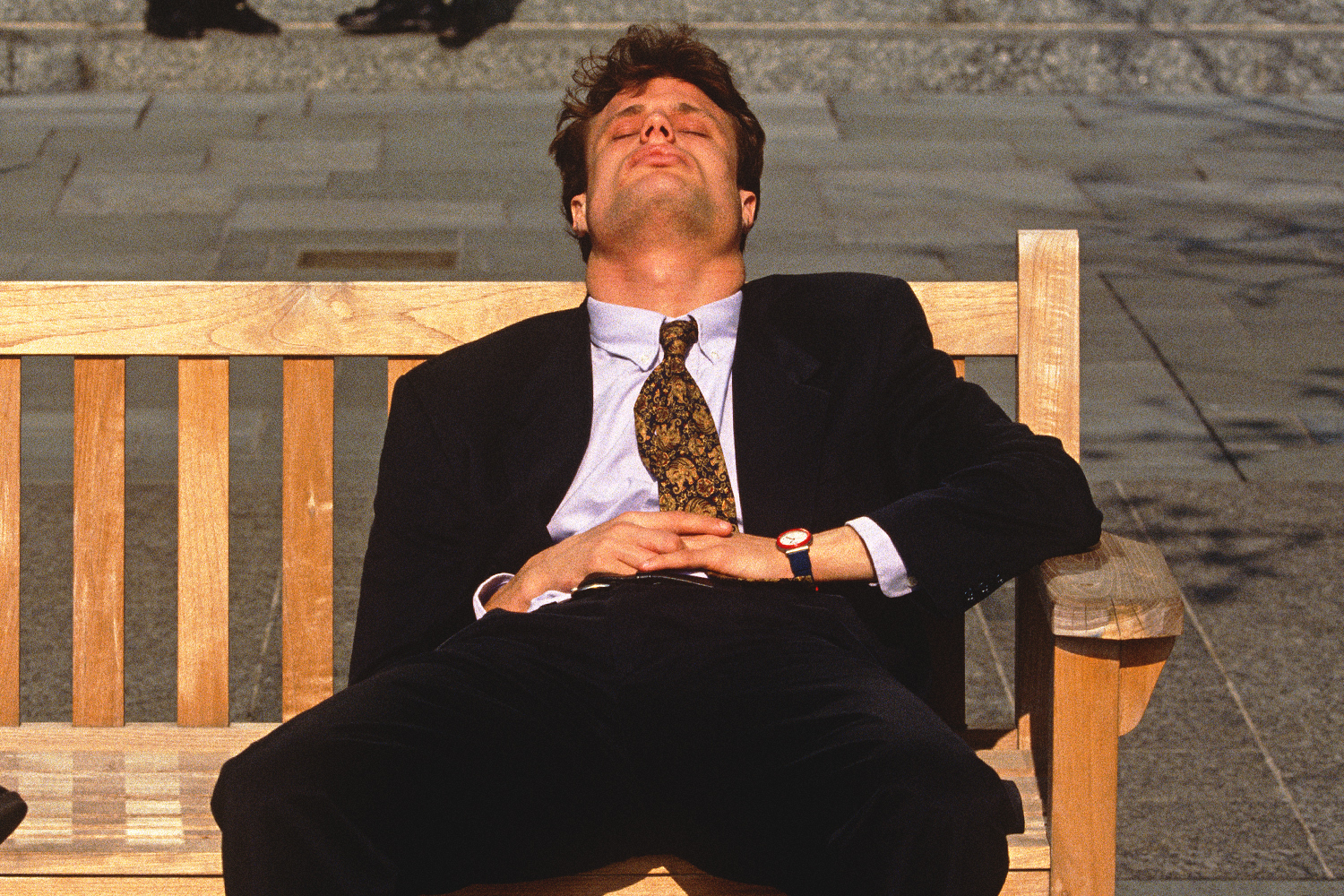 Man in business attire napping on a bench during the afternoon, symbolizing midday fatigue or energy slump at work.
