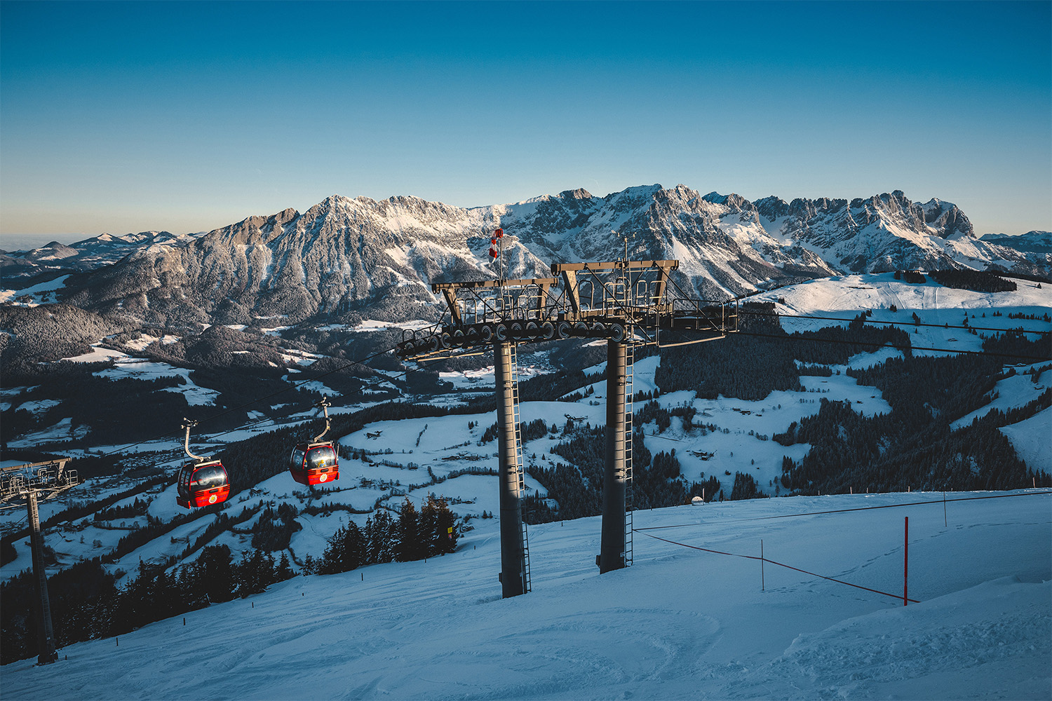 Red gondolas on a snow-covered slope at SkiWelt, Austria, on a clear winter's day.