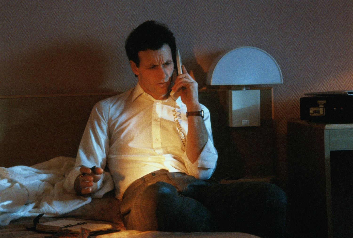 Businessman using phone in hotel room,open personal organiser on bed