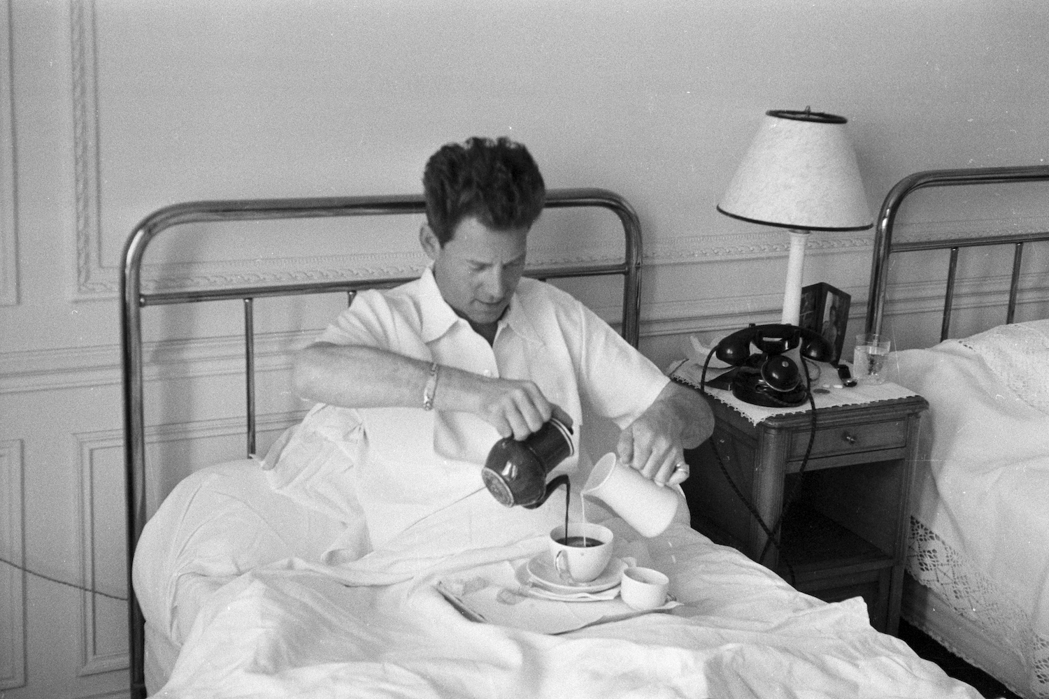 Man in bed pouring coffee and milk simultaneously with both hands
