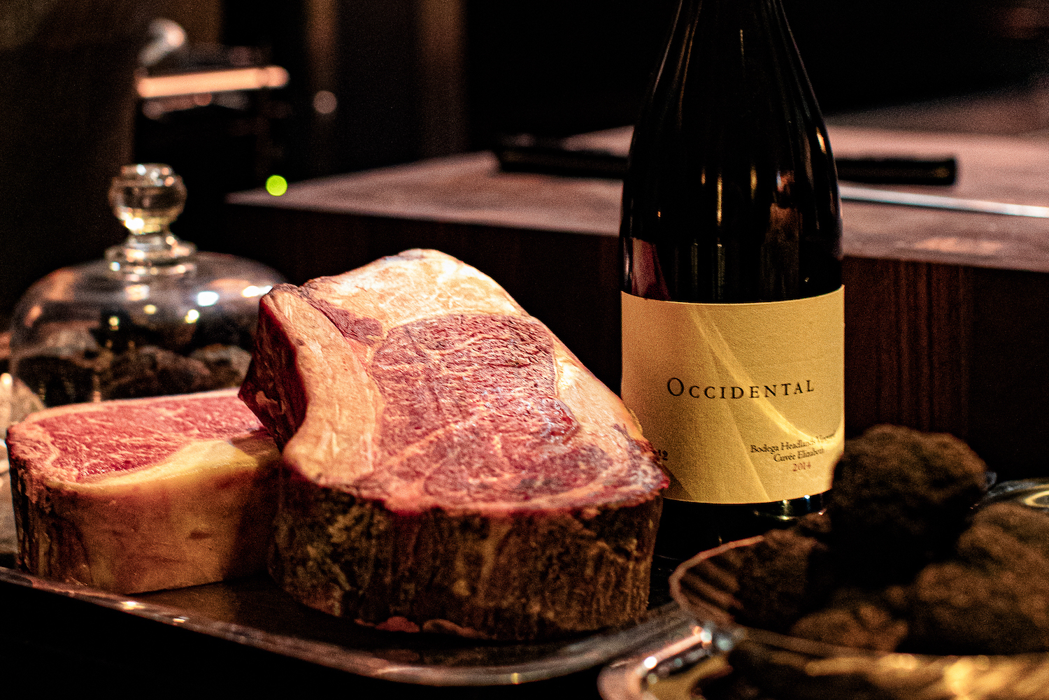 two thick steaks on a silver tray next to a bottle of red wine