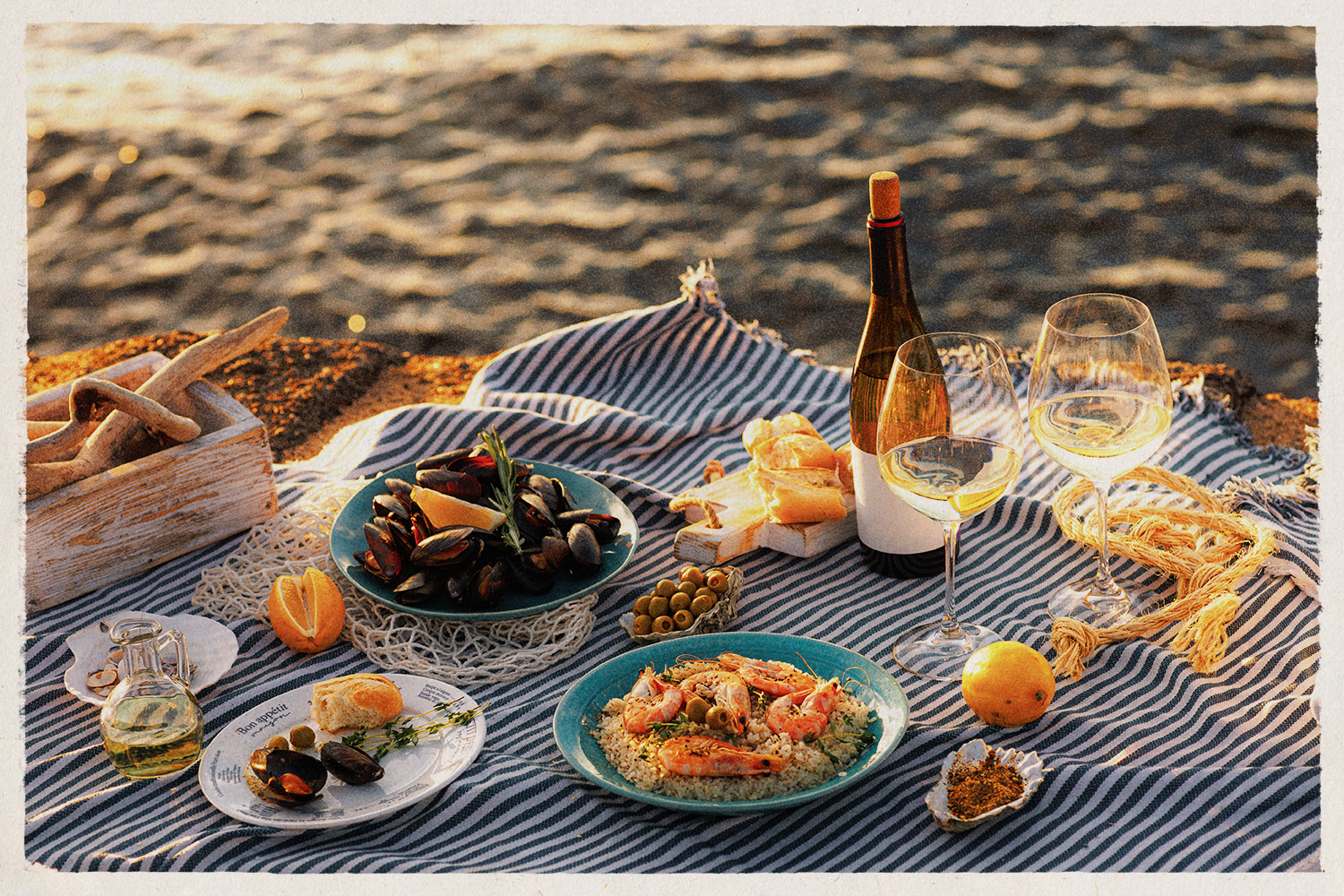 Table full of seafood and vegetable dishes and wine with the beach in the background