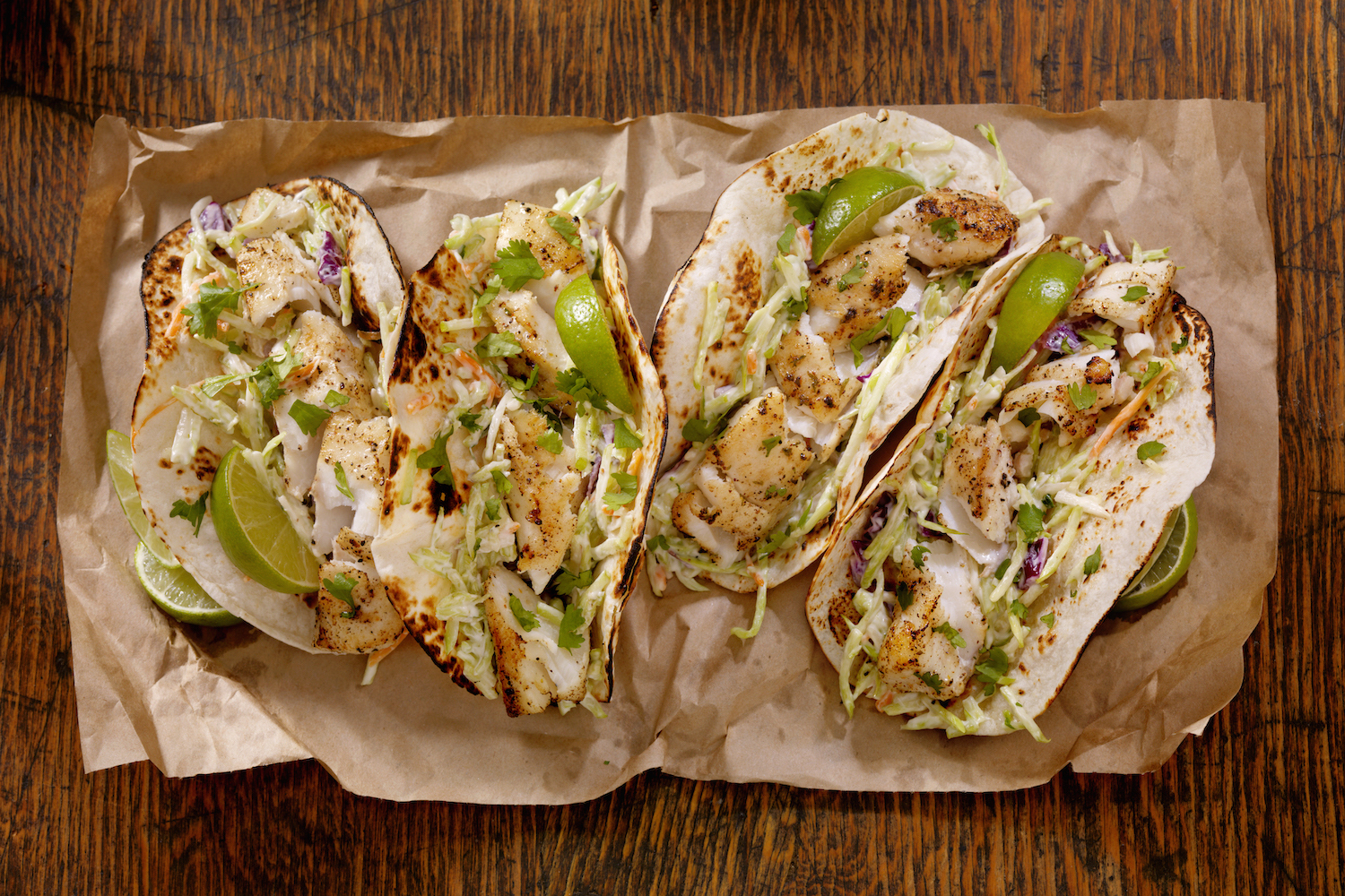 Grilled Fish Tacos with Creamy coleslaw, Lime and Fresh Cilantro on brown paper on a wooden table