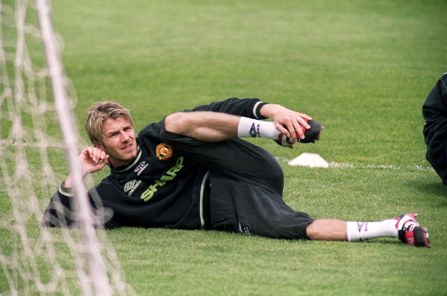 David Beckham stretching his hips on the field during a Manchester United training session, early 2000s