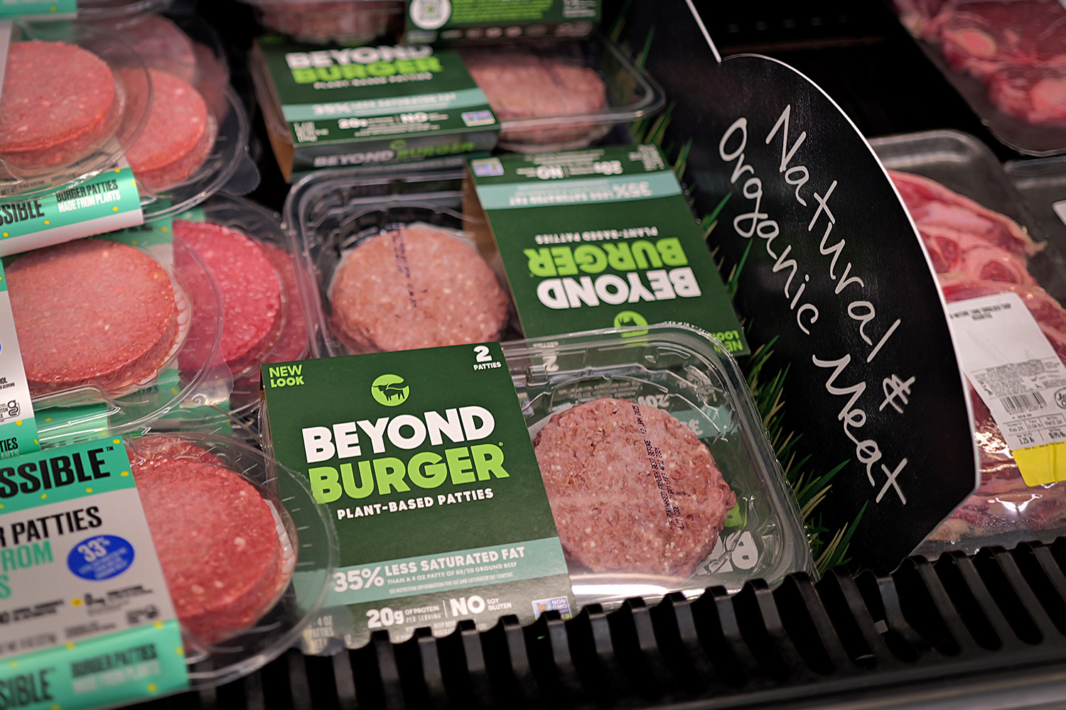 A grocery store display with Beyond Burger and Impossible Burger patties next to a sign that says "Natural & Organic Meat"