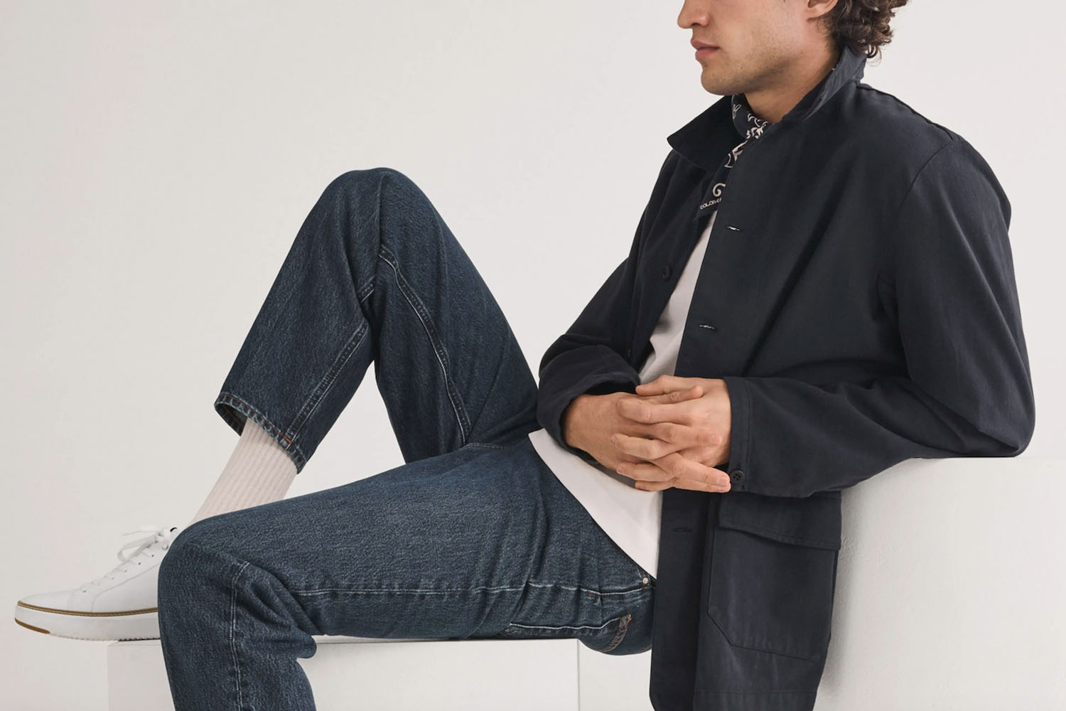 A man wearing shoes, jeans, a tee and a jacket.