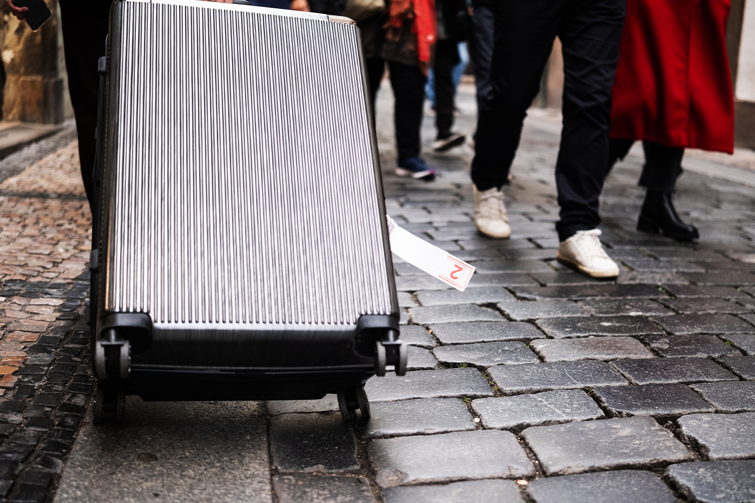 Large suitcase being dragged down cobblestone street.