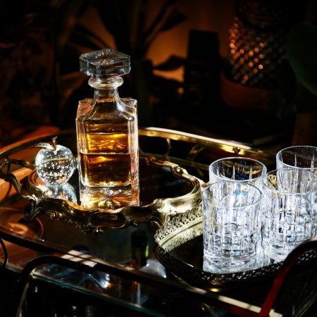 Photograph of a decanter of cask-strength bourbon and glasses sitting on a vintage bar cart in color