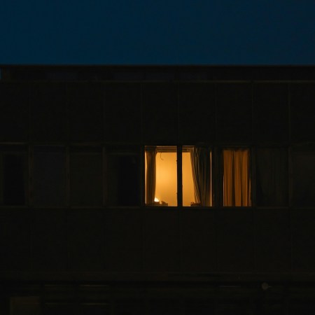 A lit bedroom window in a dark house.