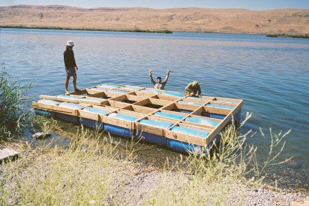 A trio of men loading a makeshift catamaran into a river.