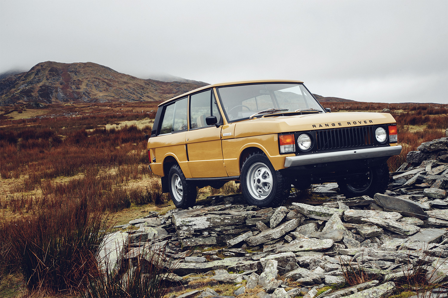 A Range Rover Classic in yellow sitting on a rocky outcrop