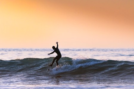 A surfer balancing on one leg while riding a wave at sunset.
