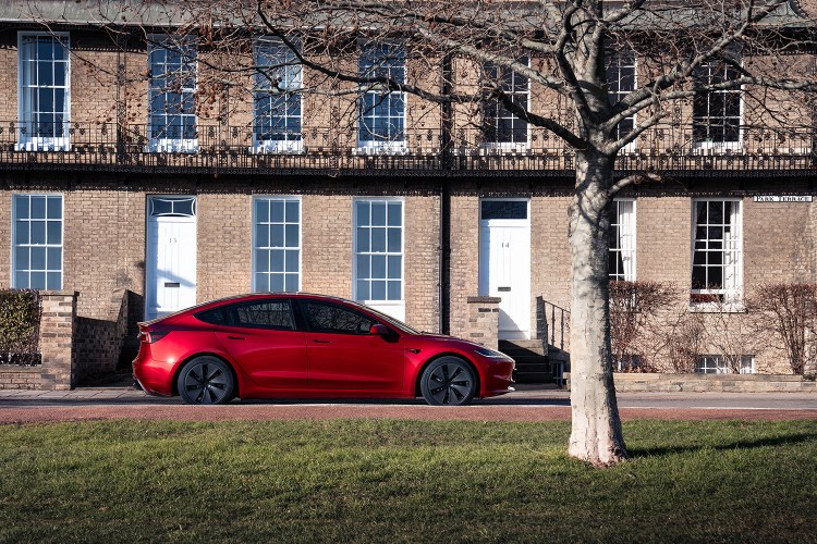A red Tesla Model 3 sitting in front of a house. New data shows the EV is the least-stolen car in the U.S.