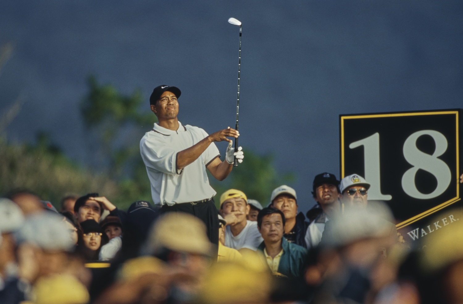 Fans surround Tiger Woods as he holds his golf swing pose.
